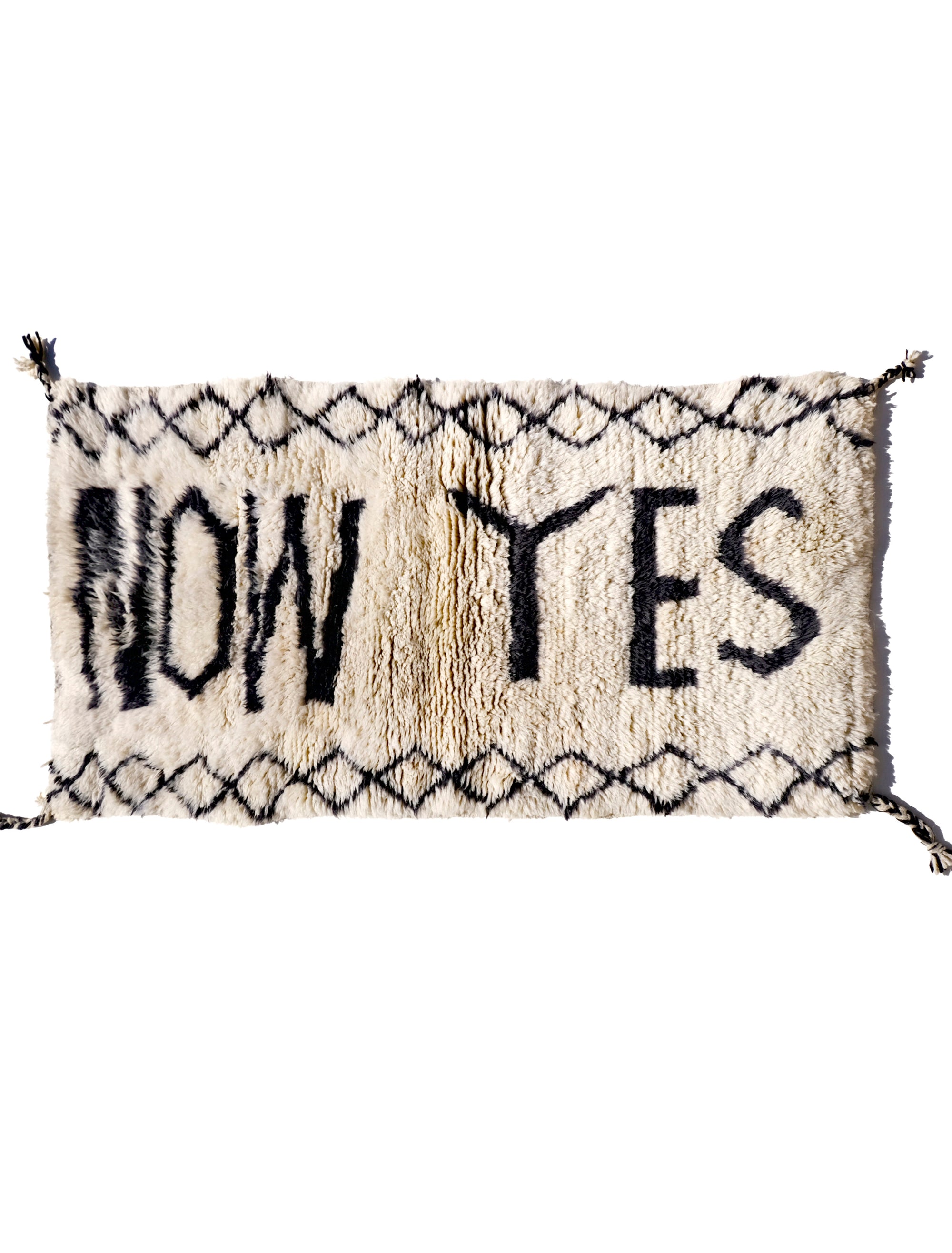 Infuse your space with positivity using the "Ivory In the Moment Rug." Handmade in the Atlas Mountains, its soft ivory base showcases the empowering phrase "NOW YES" at the center. Modern and Moroccan-inspired with small diamond patterns, this unique rug adds style and positivity to your home.